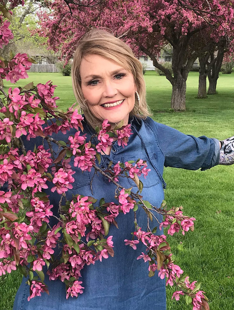 Coapt user Debbie smiling behind a blooming tree.